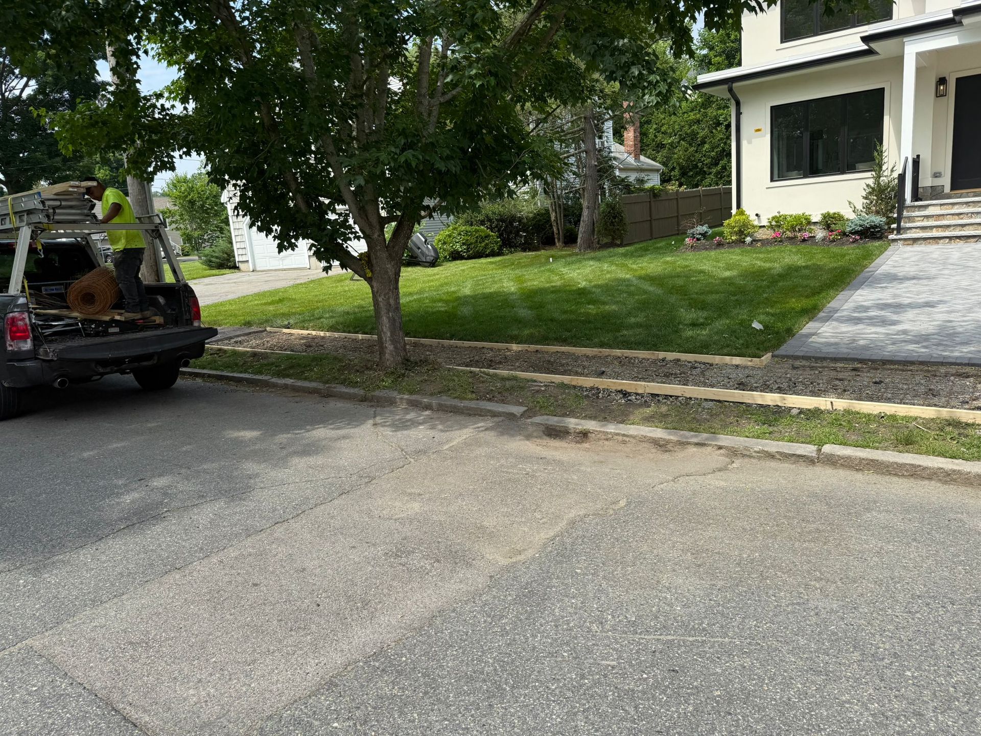 Asphalt street with a grassy yard, tree, and parked truck in front of a modern house.