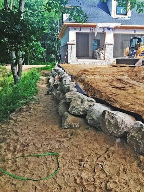 Stone retaining wall in front of a house under construction; dirt and green hose are in the foreground.