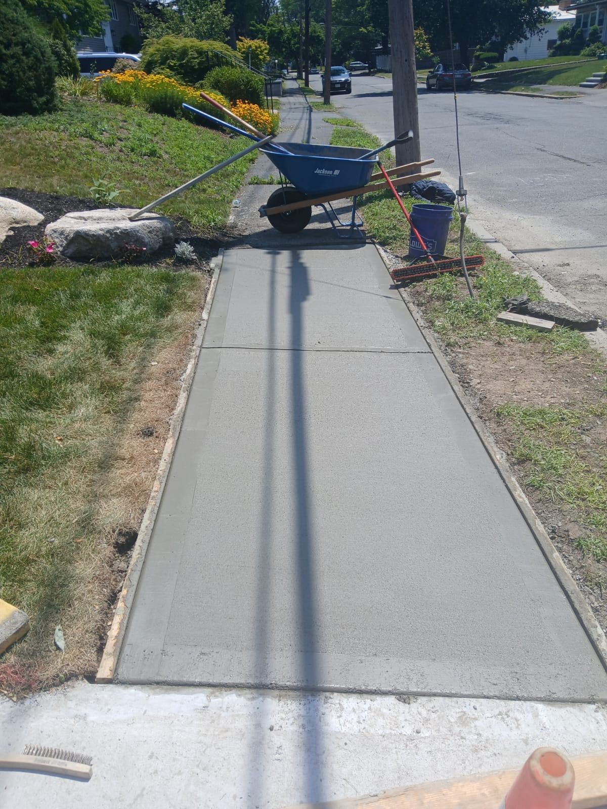 Freshly poured concrete sidewalk with a wheelbarrow and tools.