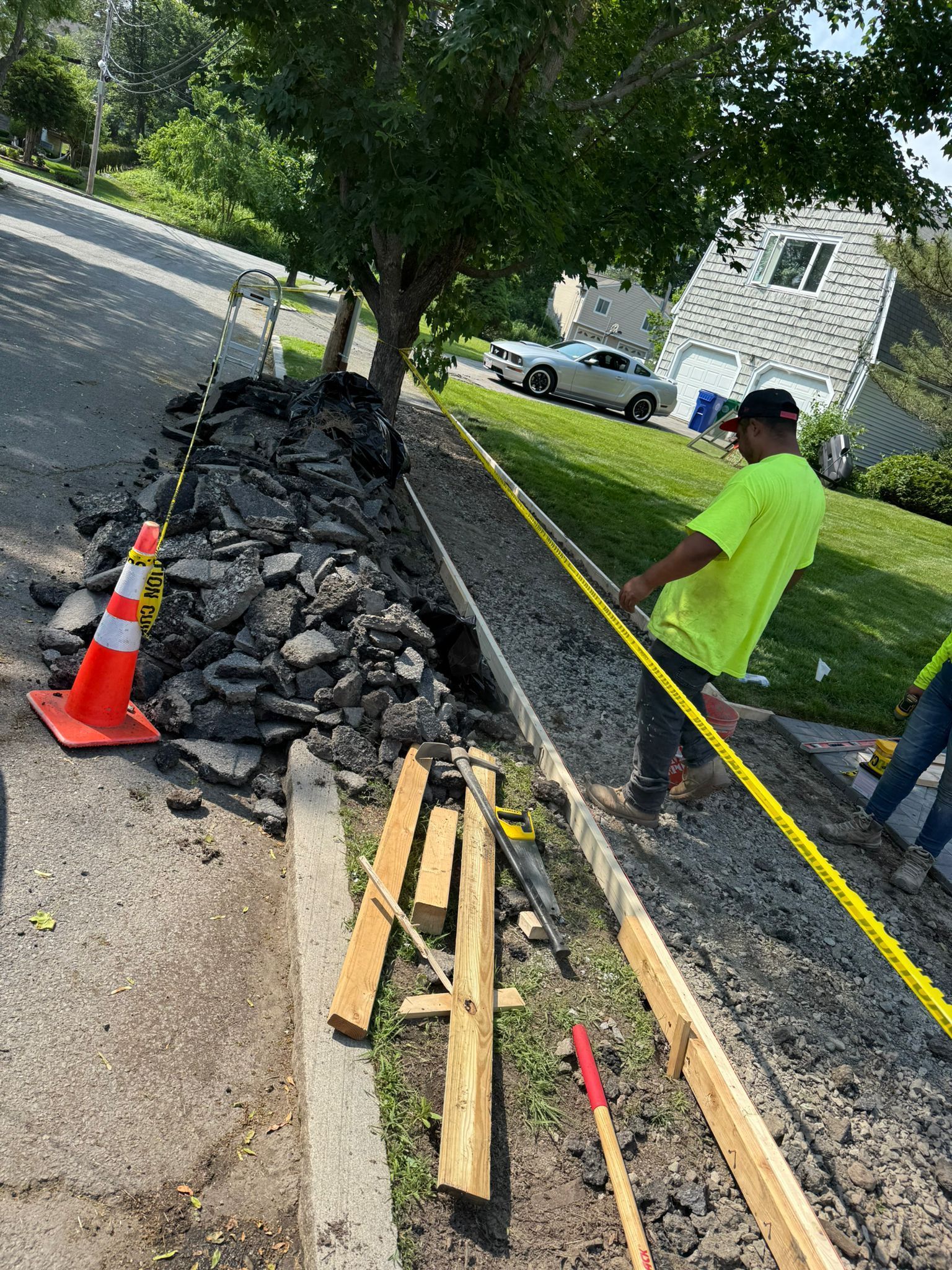Construction workers pouring concrete curb on a residential street. Debris and safety tape visible.