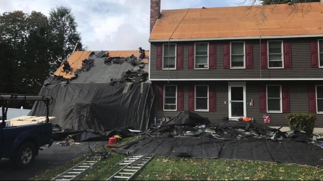 House under roof repair with tarp covering damaged area, debris on lawn, and golf cart.