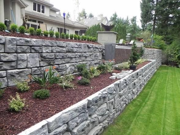 Stone retaining walls with garden beds and manicured lawn. House in background.