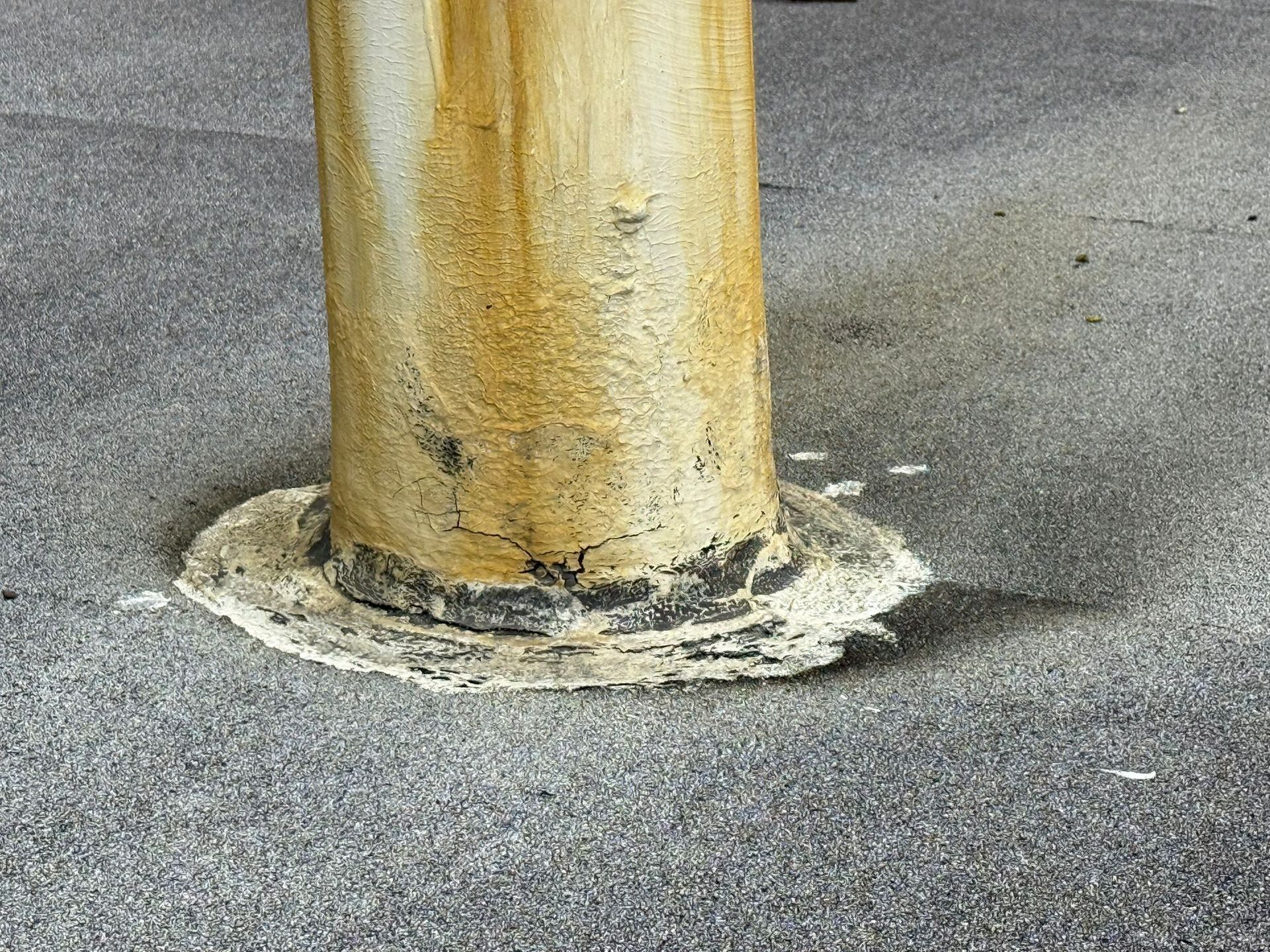 Yellow cylindrical pole on a gray asphalt surface; base is surrounded by a white sealant.
