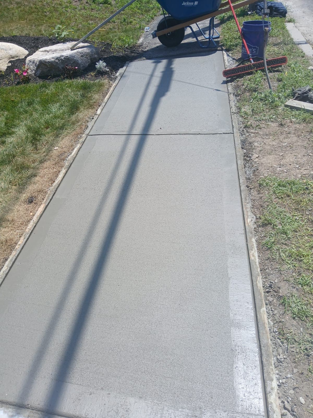 Newly poured concrete sidewalk with a wheelbarrow and tools in the background.