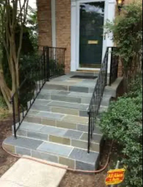 Stone steps leading up to a green door with black metal railings on either side.