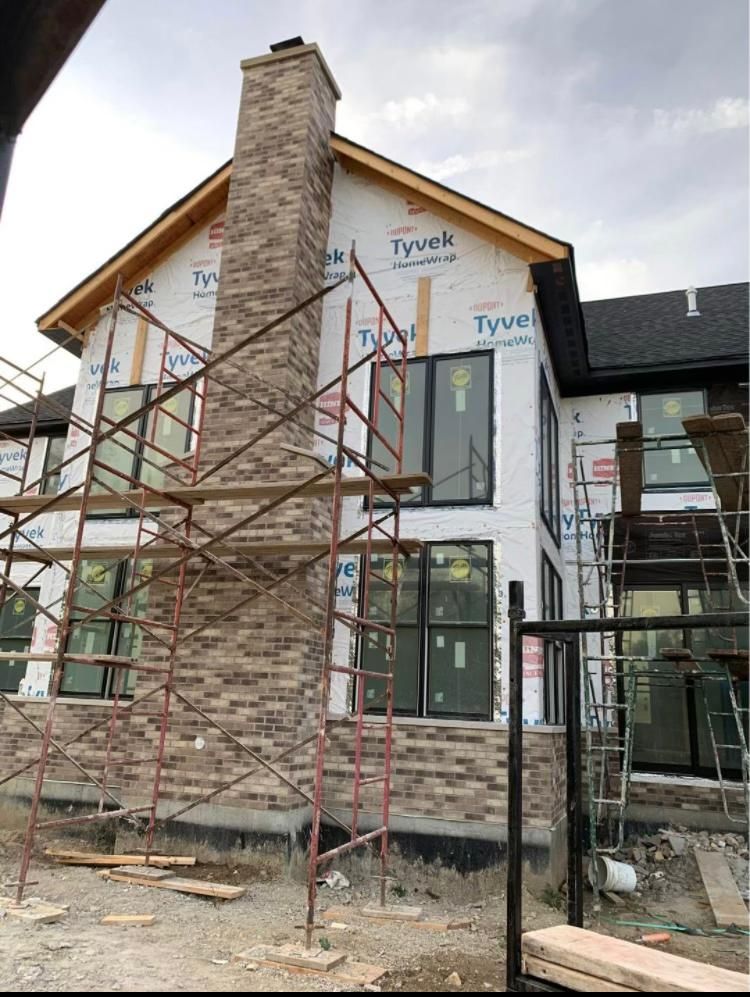 Construction of a two-story home with brick chimney, windows, and scaffolding.
