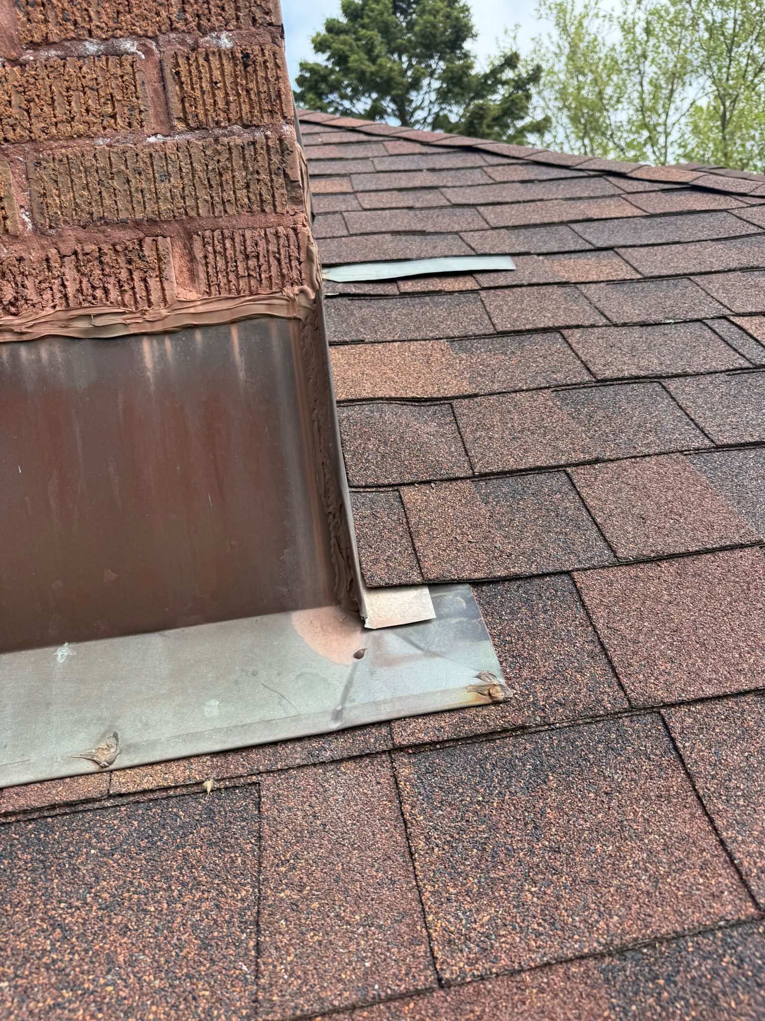 Close-up of a brown shingled roof with a chimney. Metal flashing is visible around the chimney.