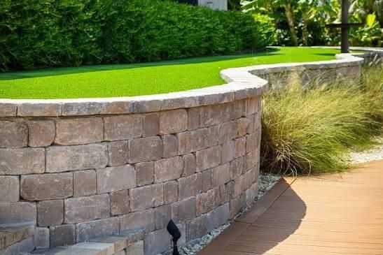 Curved stone retaining wall with green grass and foliage.