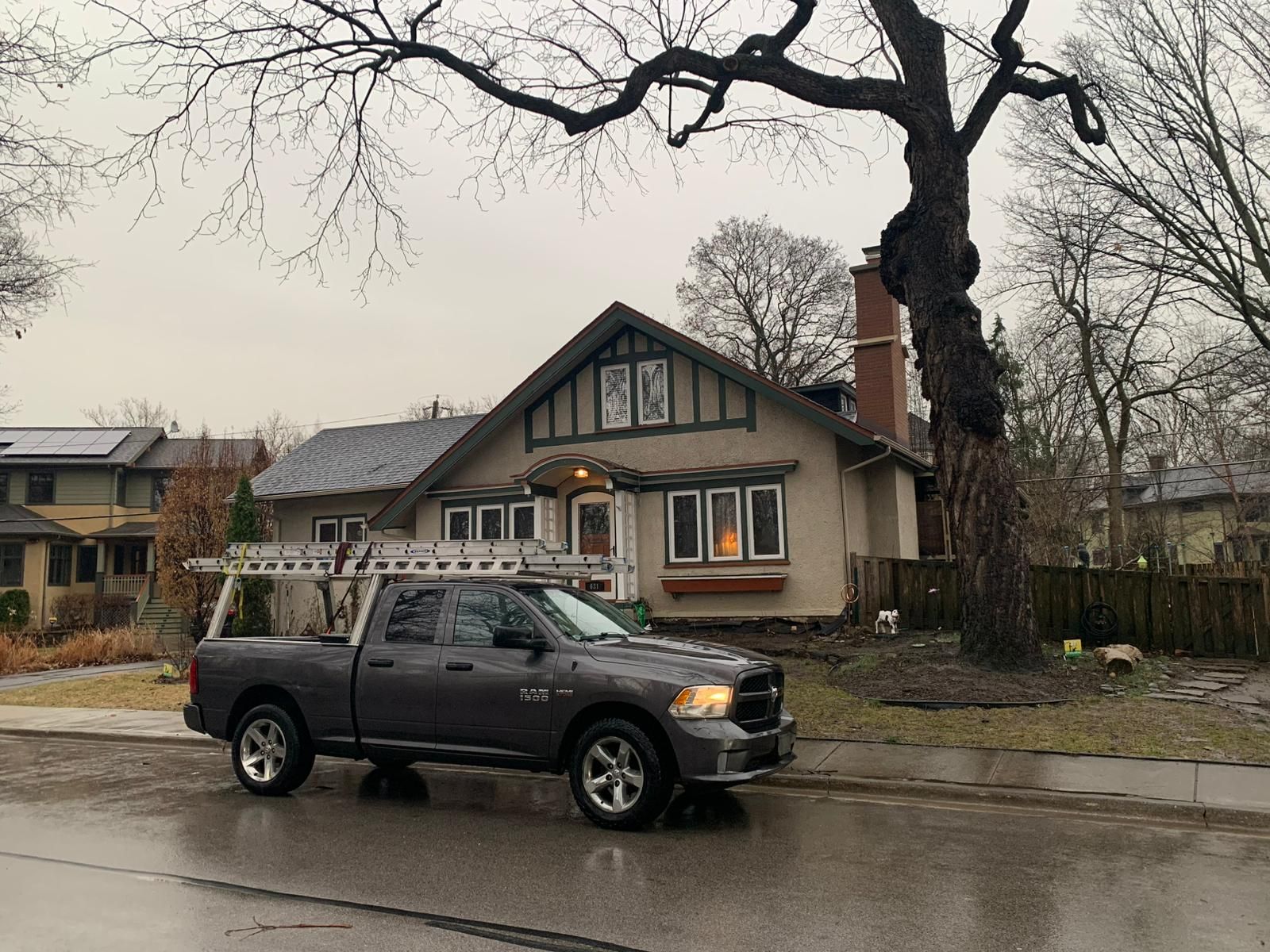 Gray truck with ladder parked in front of a house on a cloudy day.