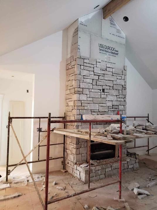 Stone veneer fireplace under construction in a room with scaffolding.