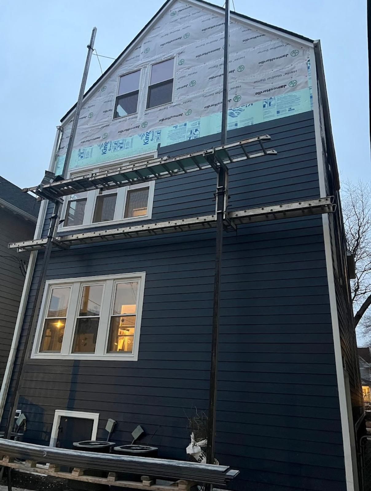 House exterior with dark blue siding being installed, scaffolding in place.