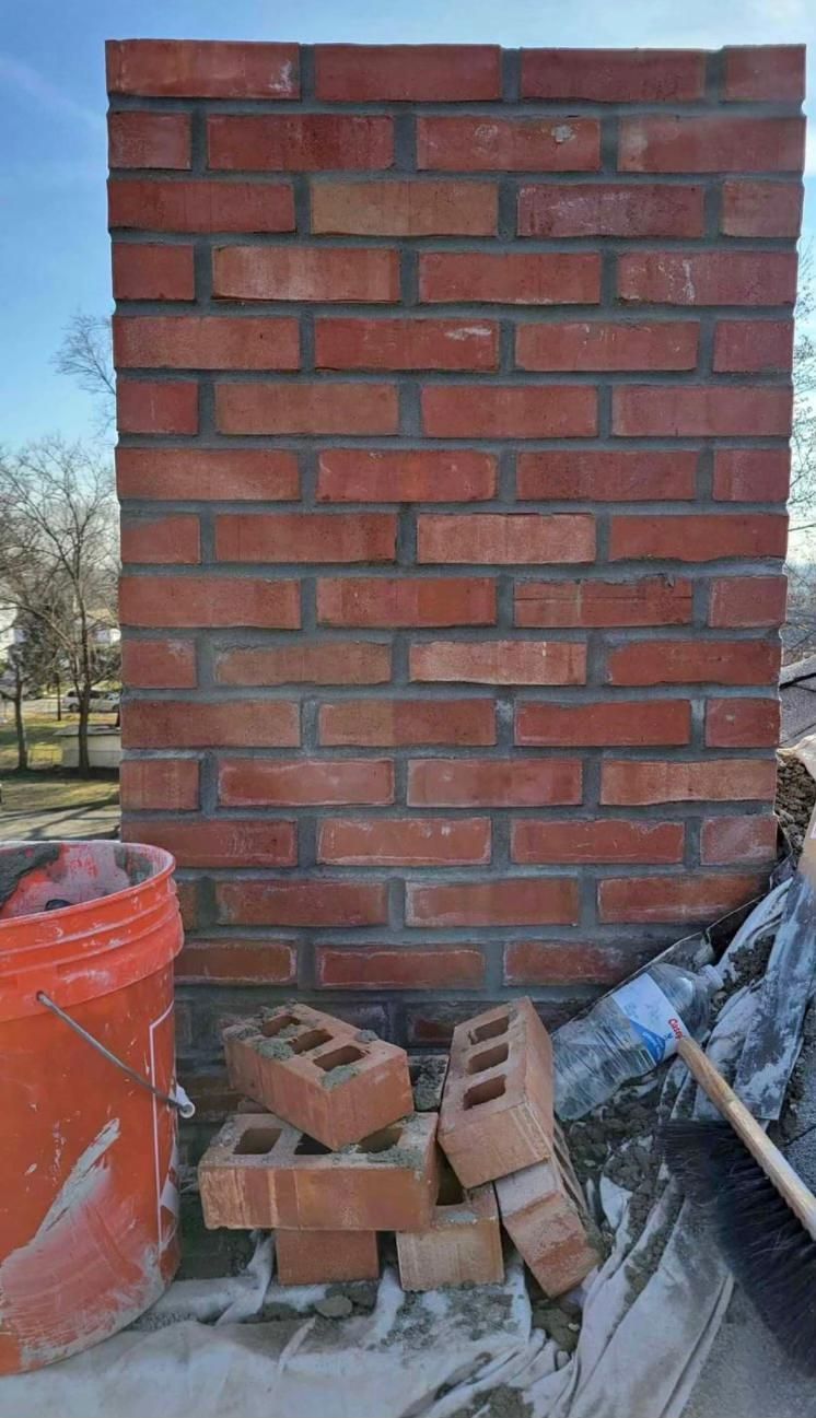 Brick chimney under construction with orange bucket, bricks, and brush.