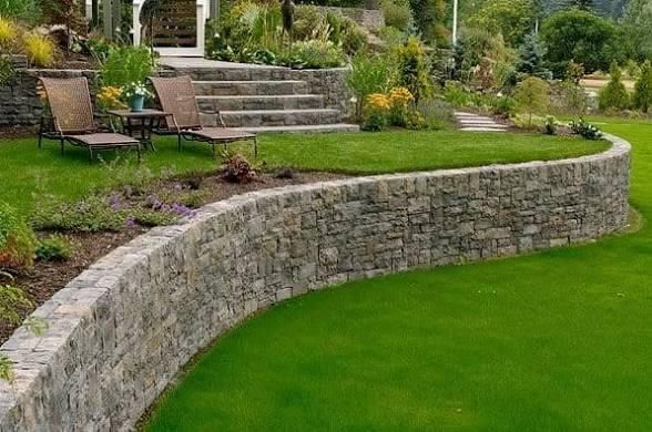 Stone retaining wall with curved shape, lush green lawn, steps leading up to a house.