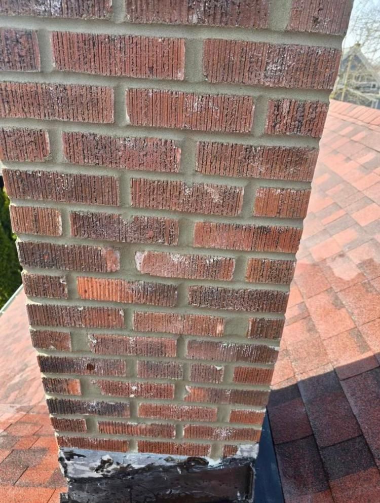 Brick chimney on a red shingled roof. Bricks are red-brown with white mortar.
