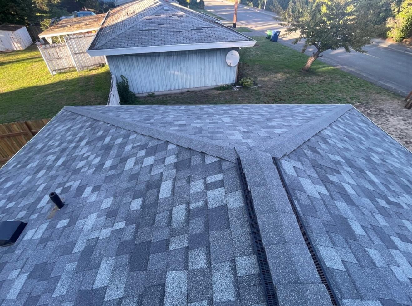 Gray shingle roof, view from above. Small shed and road in background.
