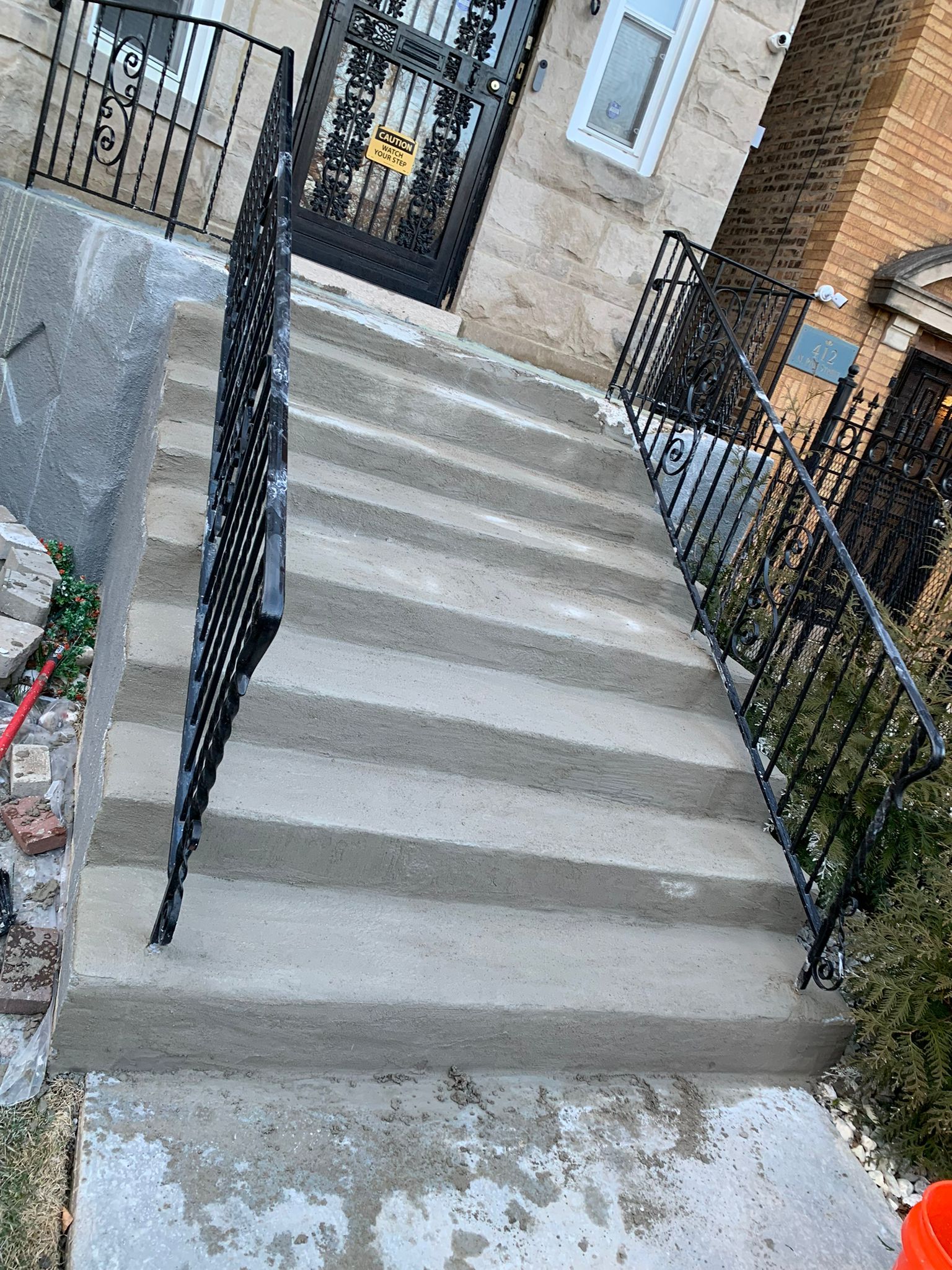 Concrete steps leading up to a house with black wrought iron railings.