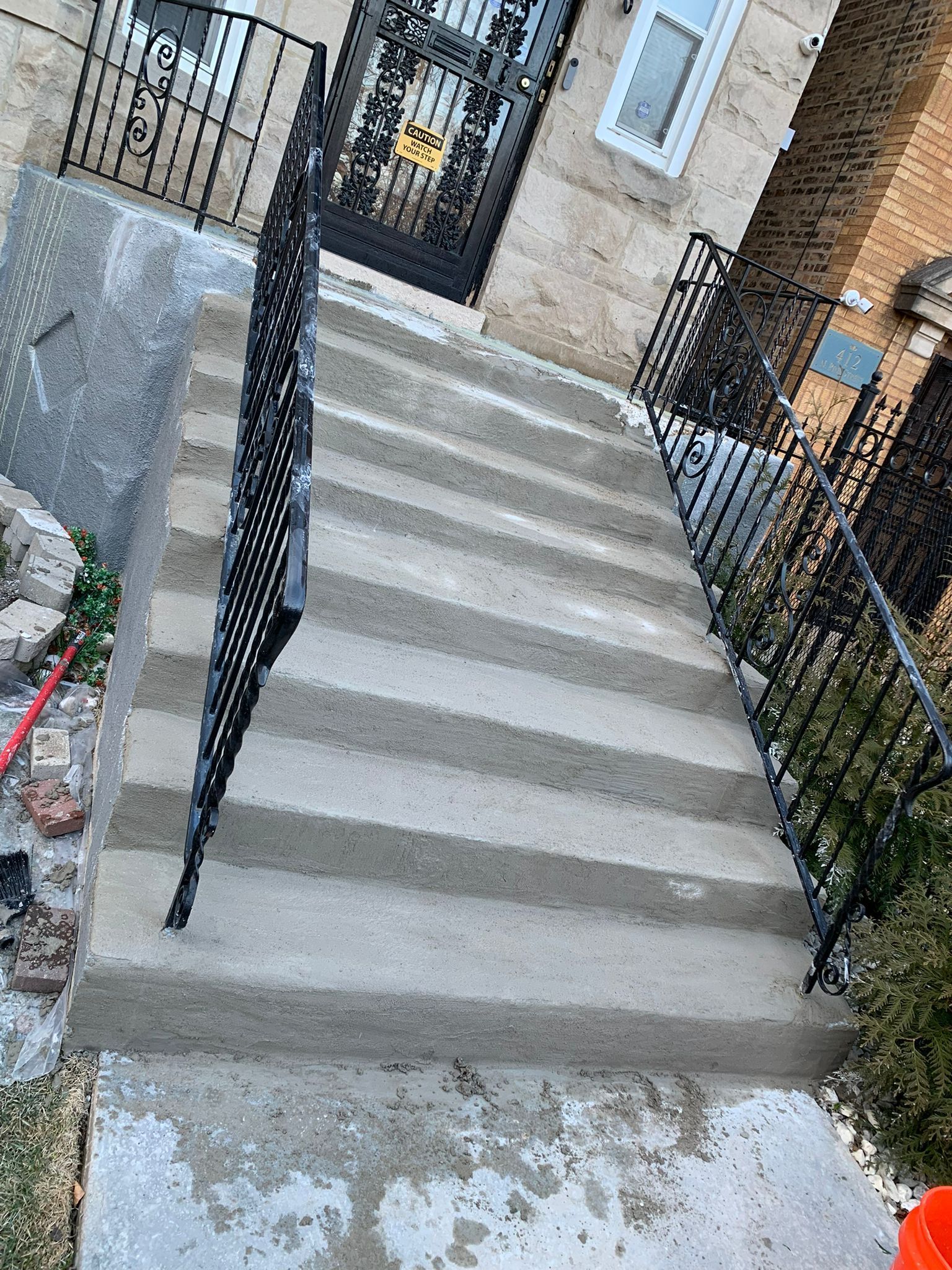 Concrete front steps leading to a doorway, with black metal railings on either side.