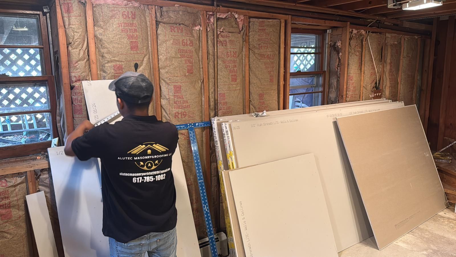 Man installing drywall on a partially constructed wall near windows