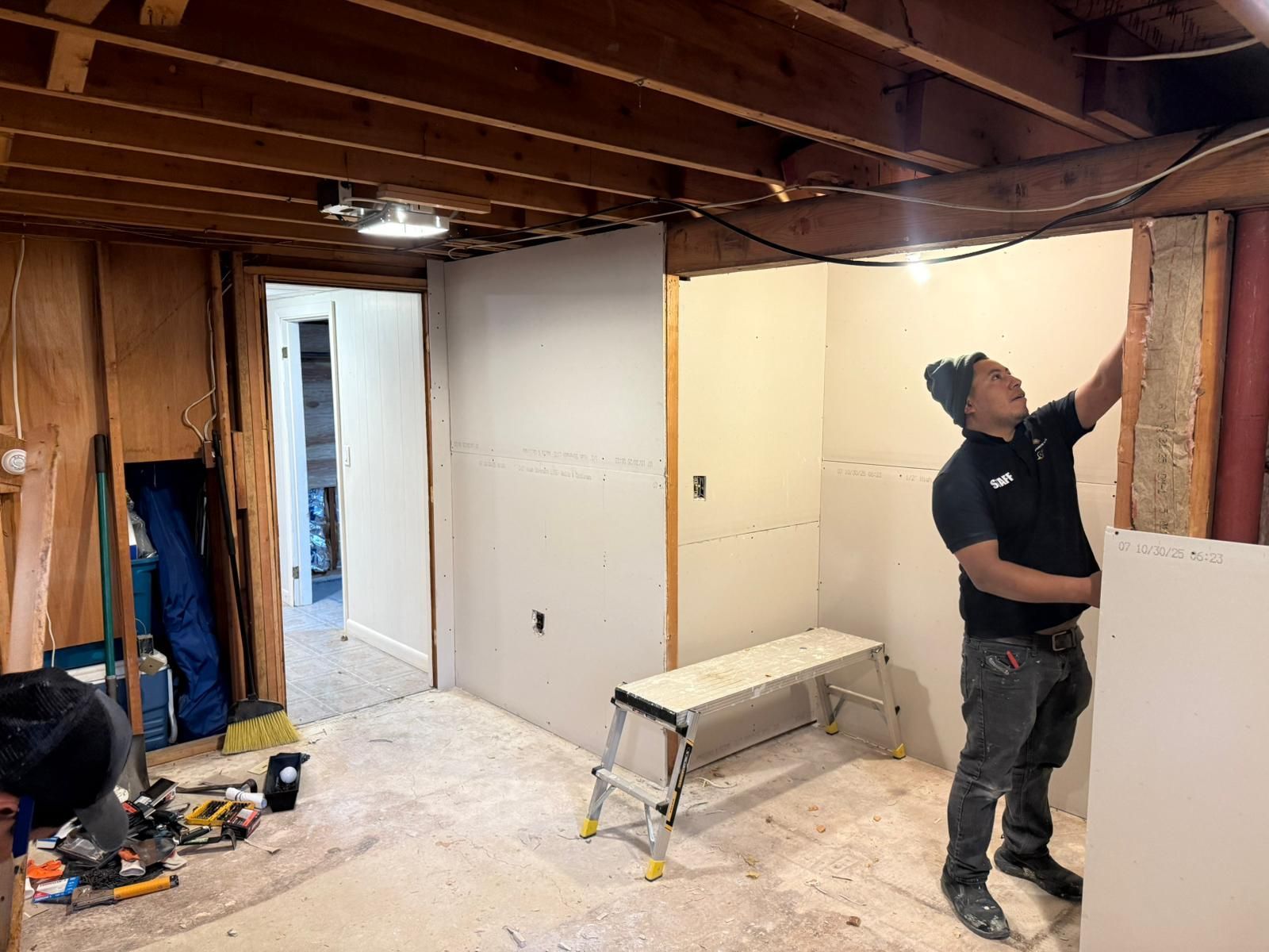 A person installing drywall in a basement