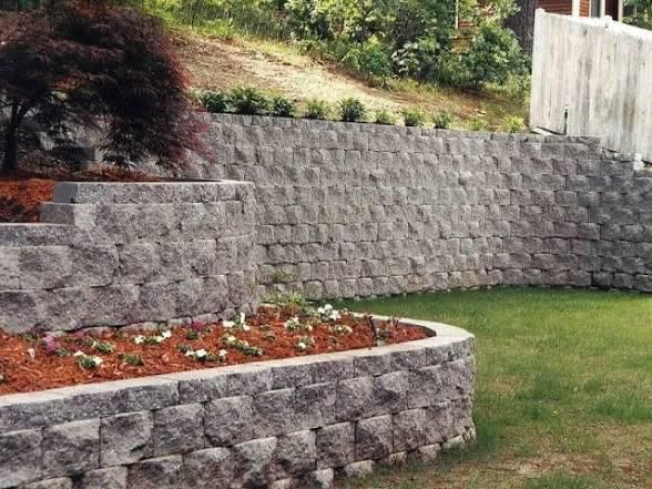 Gray stone retaining walls terraced into a hillside, with a small flower bed in the foreground.