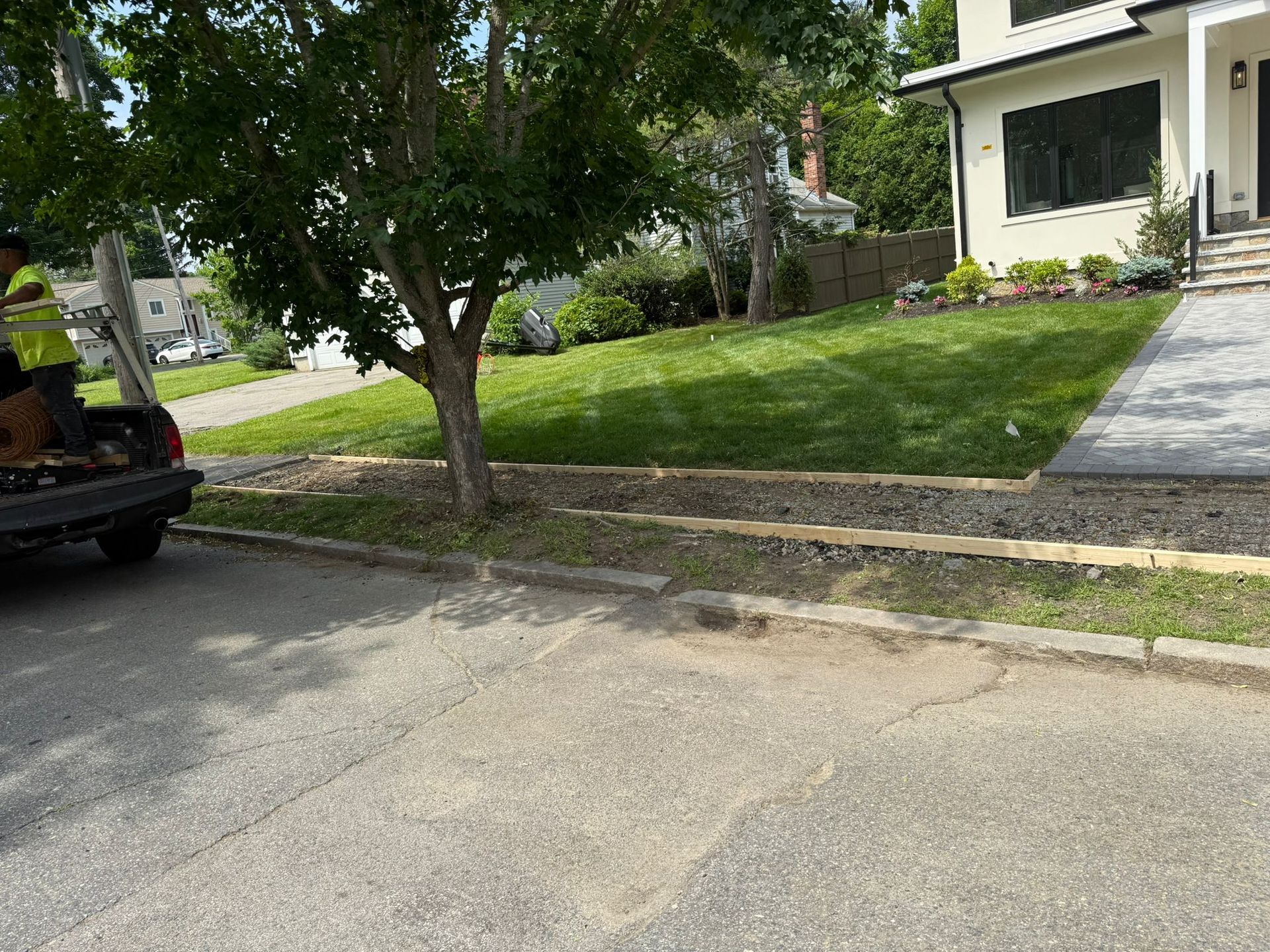 A black truck parked on a street near a house with a well-maintained lawn and tree.