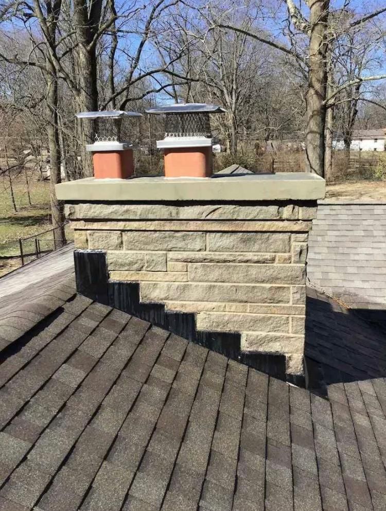 Stone chimney with two terracotta pots and wire mesh caps, on a shingled roof.