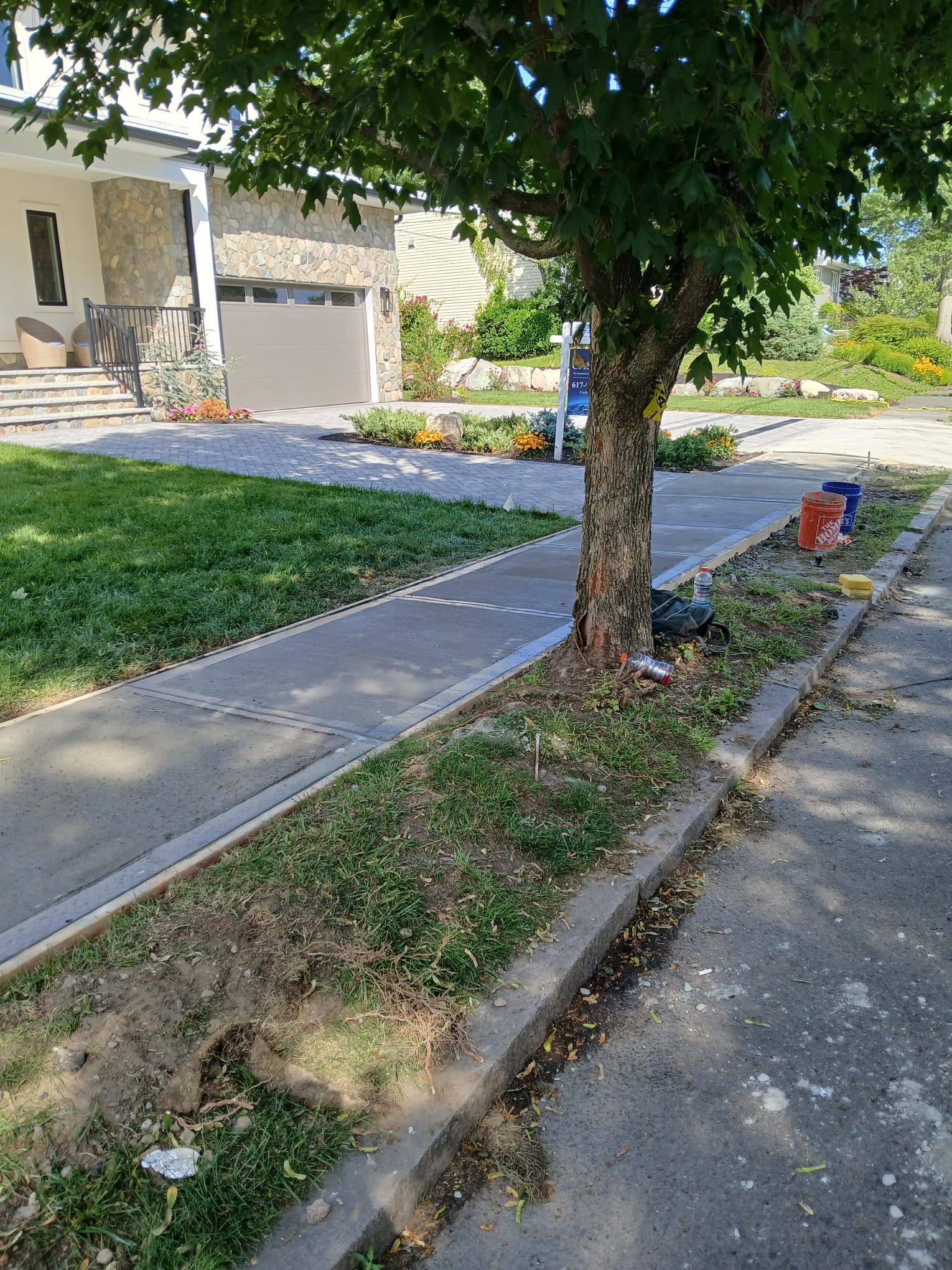 Sidewalk next to a tree and lawn, leading toward a house with a garage.