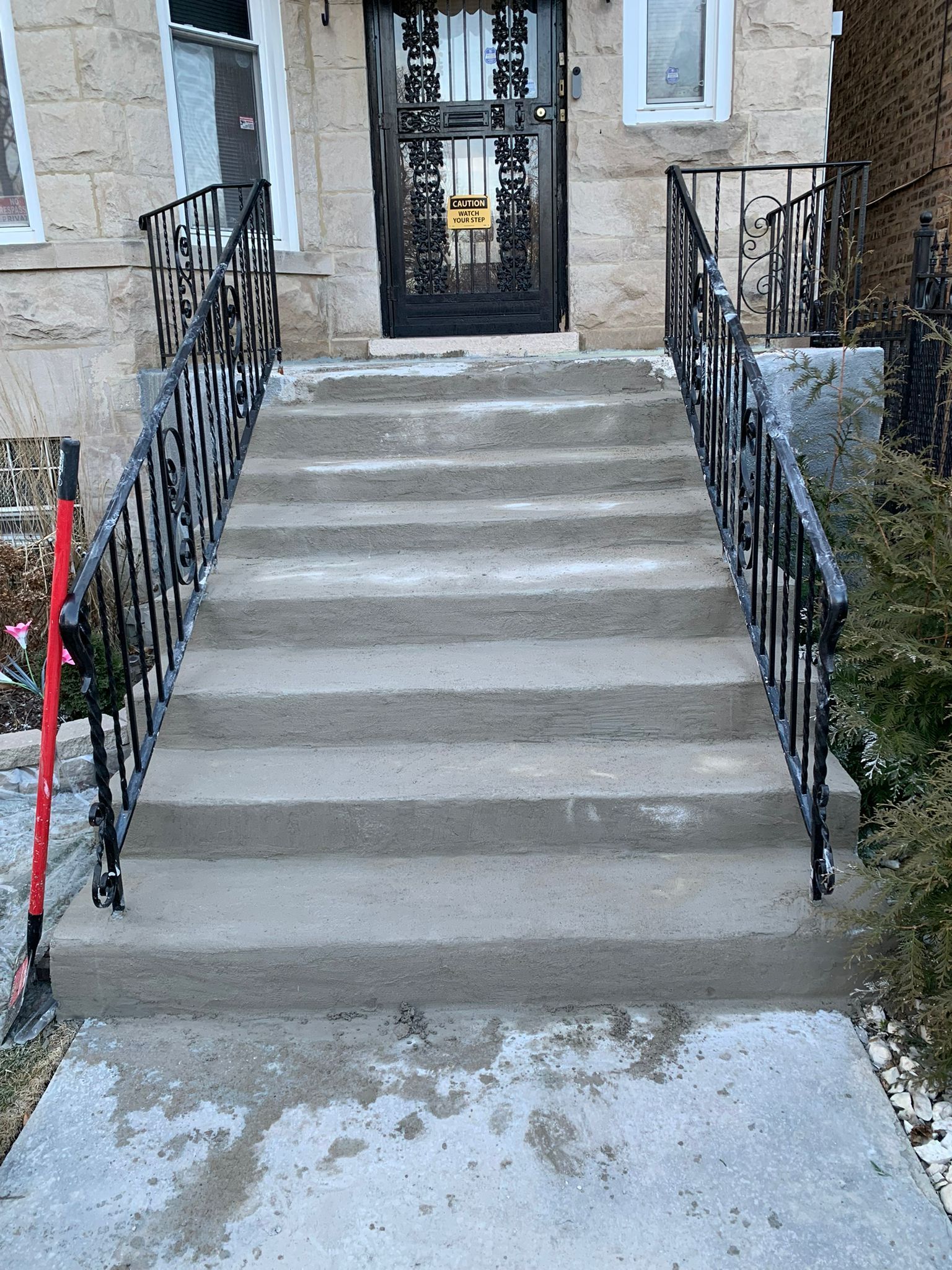 Concrete steps leading to a building's entrance. Black wrought iron railings on both sides.