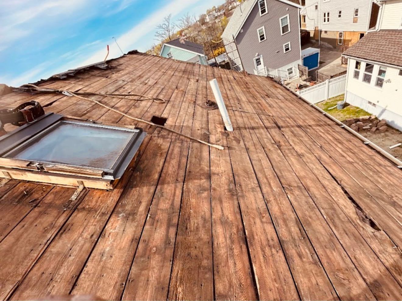 Wooden roof with a skylight and buildings in the background.