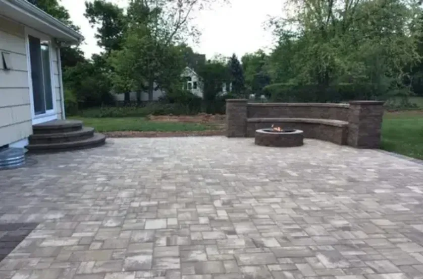 Brick patio with built-in seating, fire pit, and stairs leading to a house with a sliding glass door.