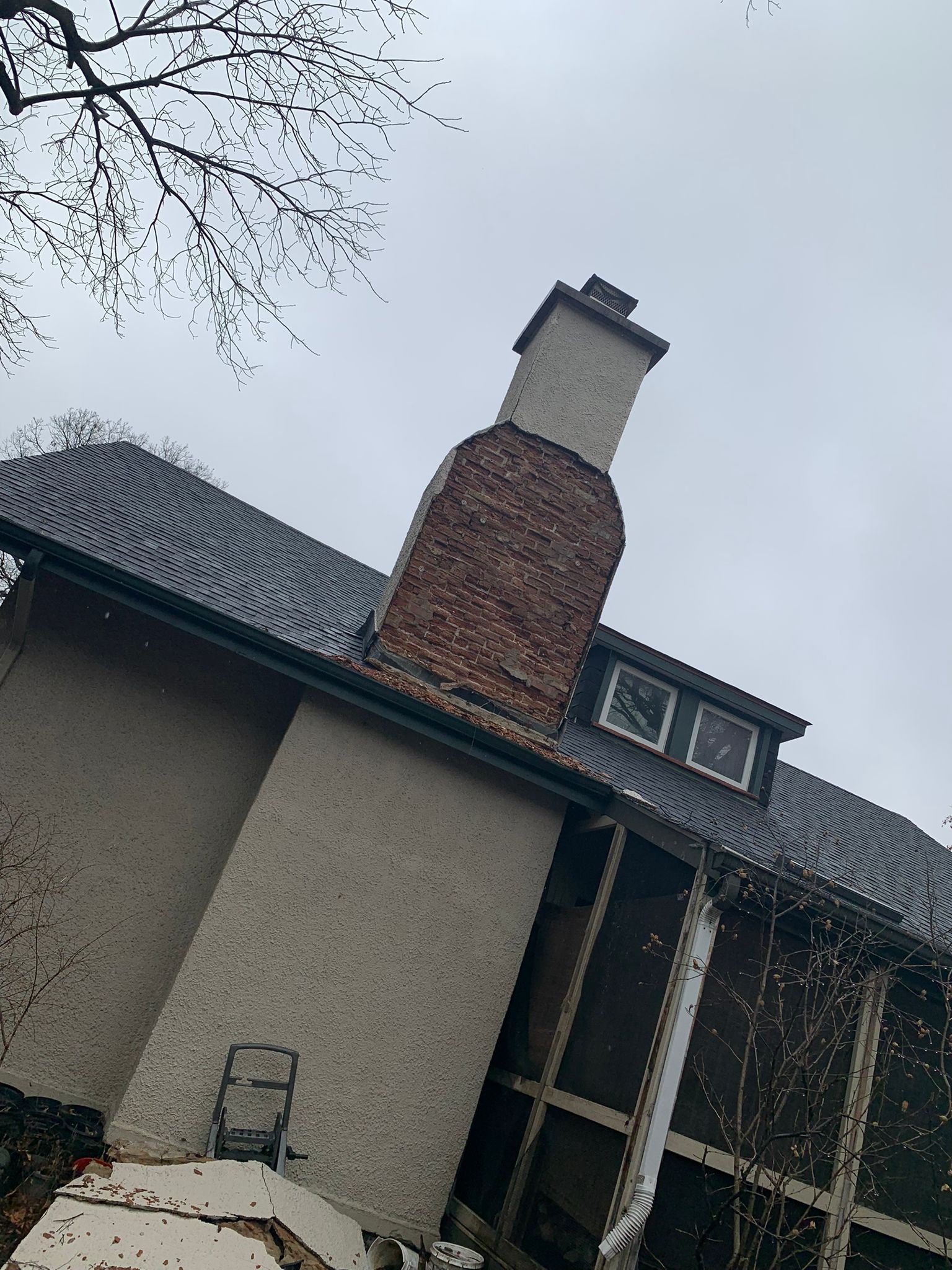 Brick chimney on a house with a gray roof and stucco walls, under an overcast sky.