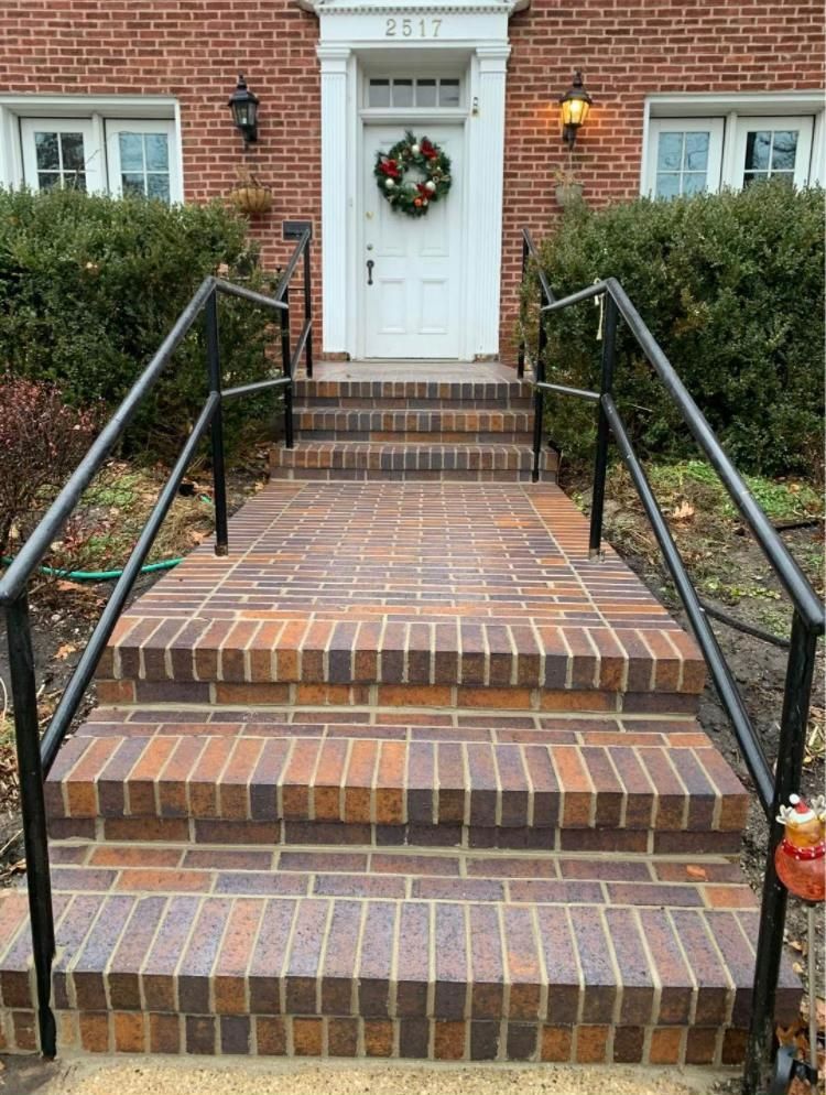 Brick steps leading to a white door with a wreath. Black railings on either side.