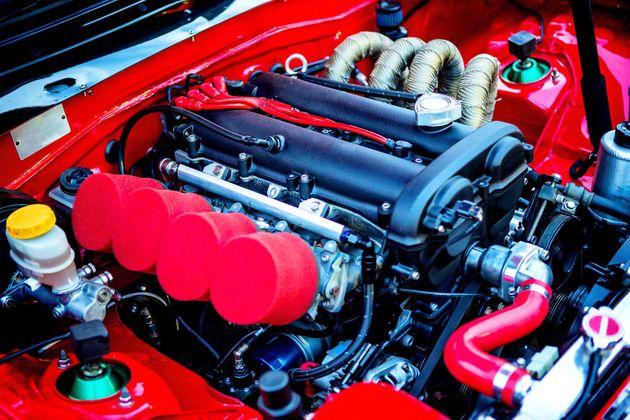A high-performance car engine with red air filters, a black engine cover, and red silicone hoses in a red engine bay.