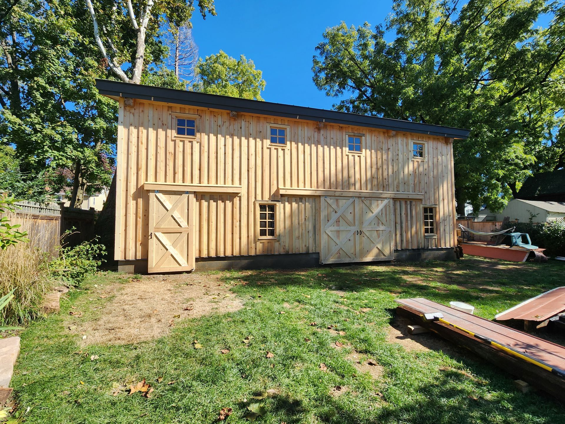A wooden barn is sitting in the middle of a lush green field.