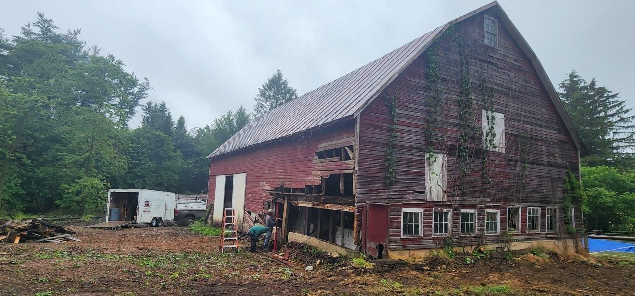 A large red barn before in the middle of a field surrounded by trees.