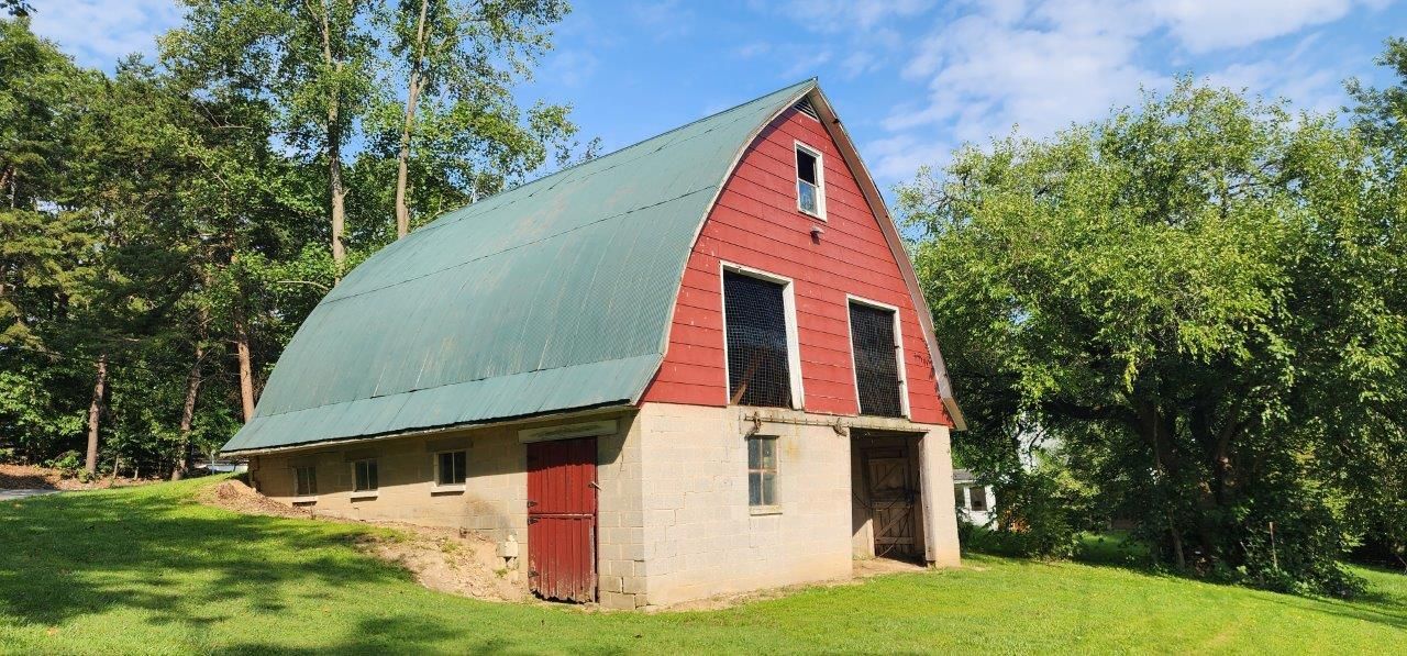 A red barn before with a green roof in the middle of a grassy field.