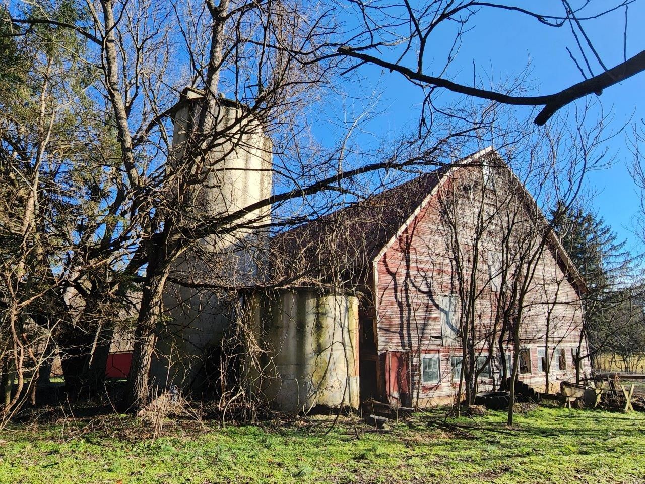 A red barn before is sitting in the middle of a grassy field surrounded by trees.