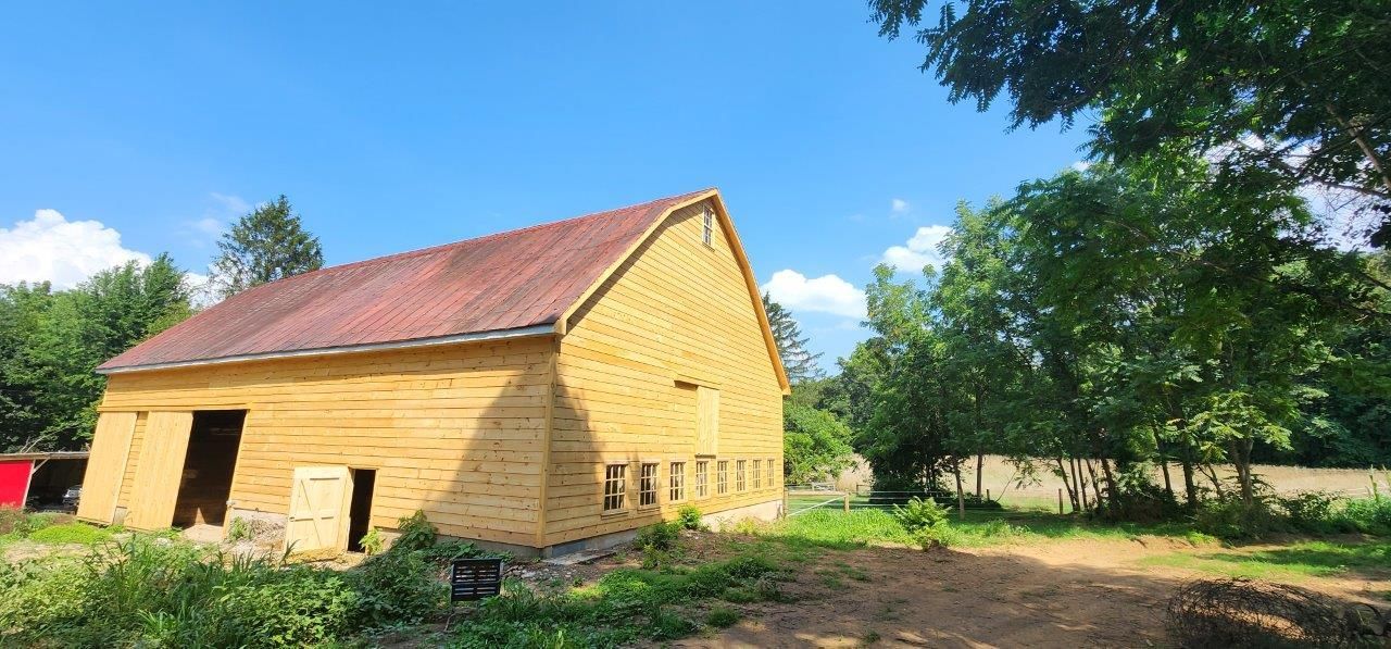 A restored barn in the middle of a grassy field surrounded by trees.
