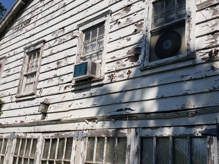 A white house with peeling paint and a fan on the side