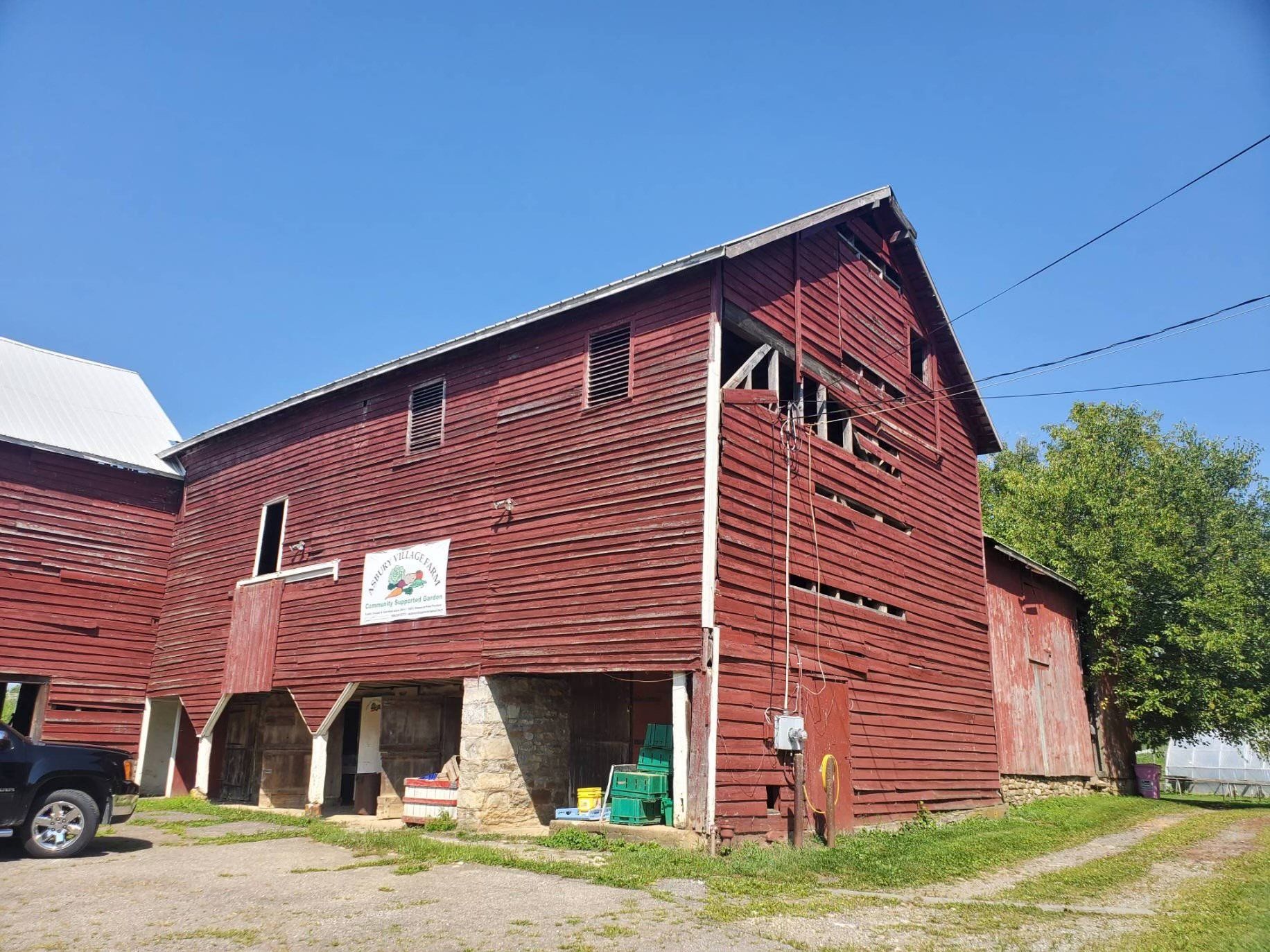 A red barn with a truck parked in front of it on a sunny day.