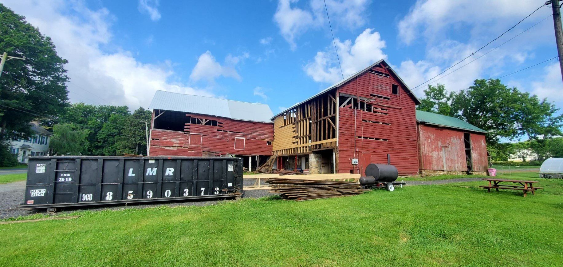 A large red barn is being demolished and a dumpster is in front of it.