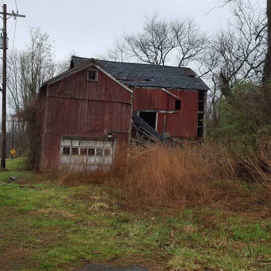 An old red barn is sitting in the middle of a grassy field.