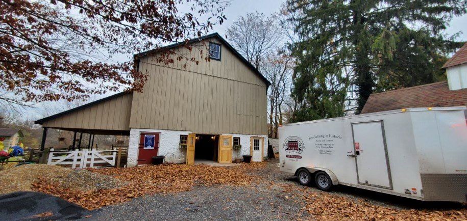A white trailer is parked in front of a barn.
