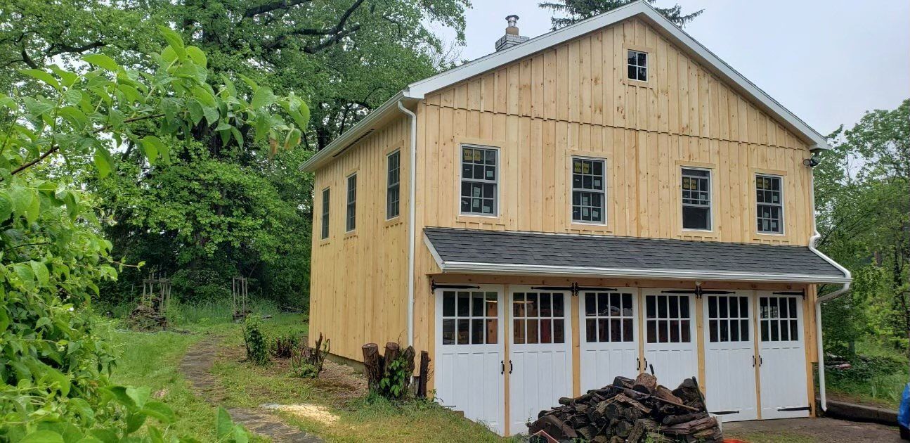 A large wooden barn with white doors and windows is surrounded by trees.