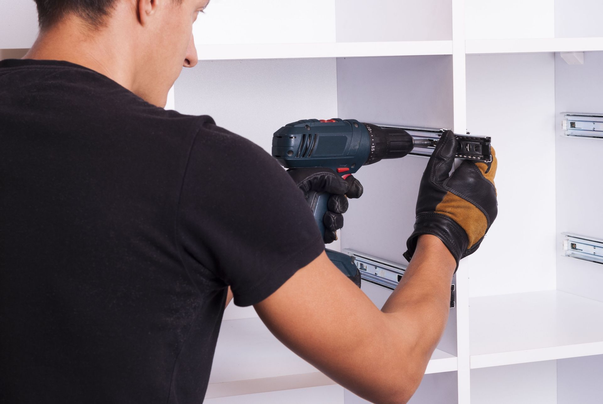Person in black shirt using a power drill to install drawer slides inside a white cabinet.