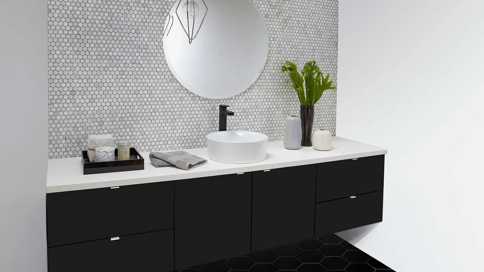 Modern bathroom with black vanity, white countertop, round mirror, and patterned tile wall.