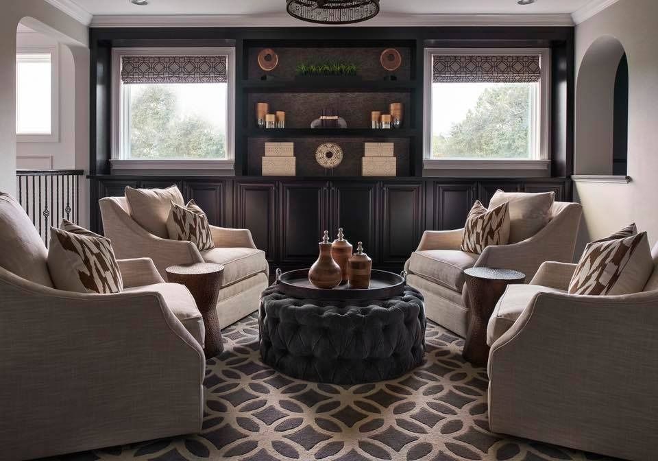 Cozy seating area with four armchairs around a circular ottoman on patterned rug, dark wood cabinetry in background.