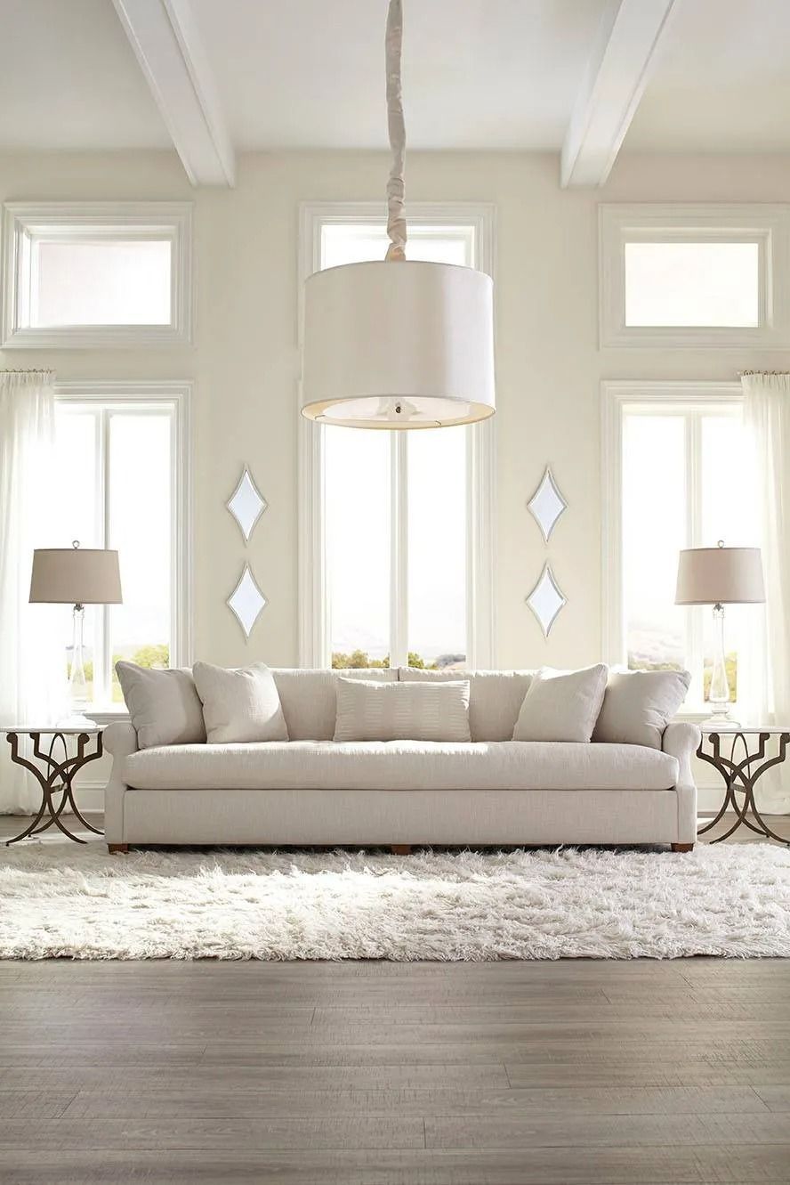 Spacious living room with white sofa, rug, and pendant light. Two side tables, large windows.