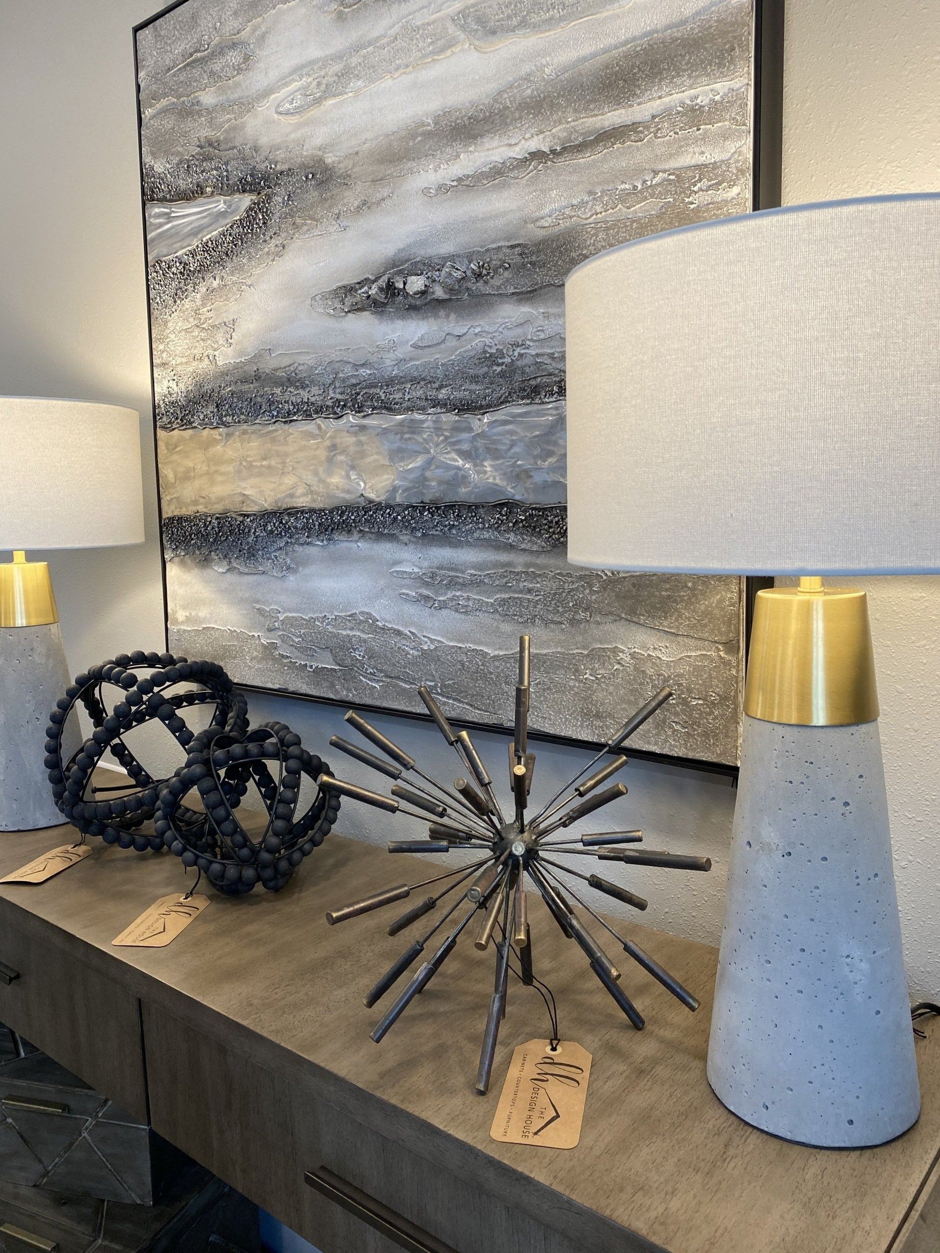 Display of decorative items on a console table, including lamps, art, and metallic sculptures; neutral colors.