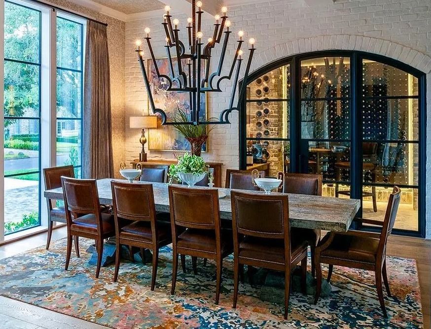 Dining room with long wooden table, leather chairs, ornate chandelier, and arched wine cellar.